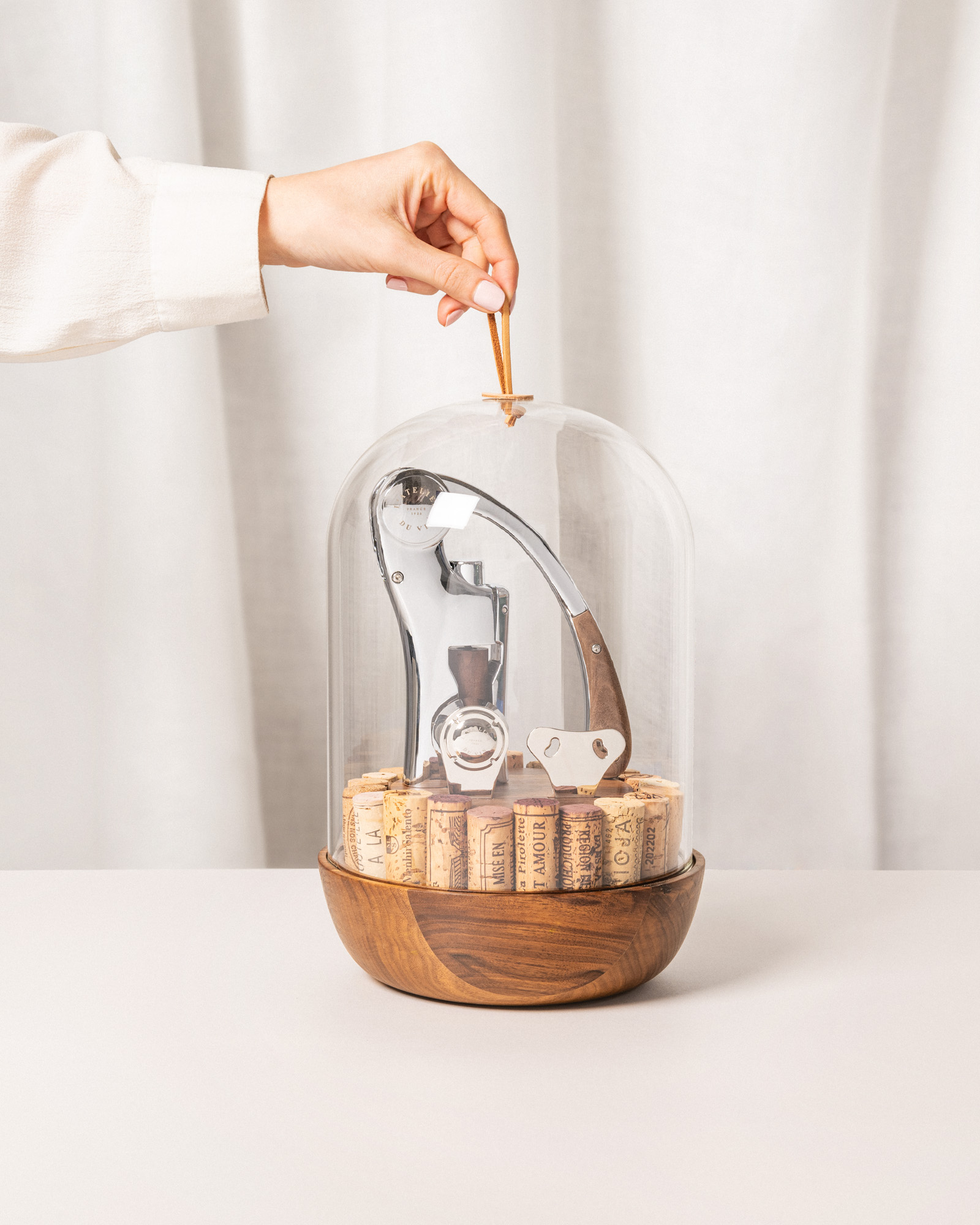 Coffret sommelier avec une main qui soulève délicatement la cloche en verre soufflée qui dévoile les outils du vin