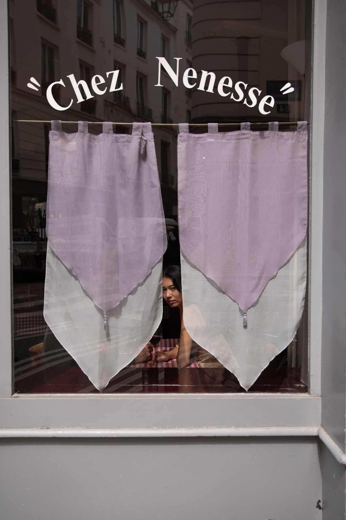 Vue de la devanture de Chez Nenesse à Paris, avec une scène de dégustation de vin aperçue à travers la fenêtre.