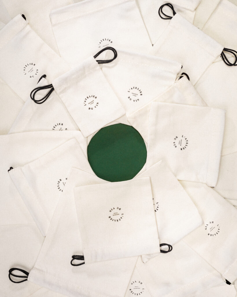 Ensemble de pochons en coton écru L’Atelier du Vin disposés en cercle autour d’un centre vert.